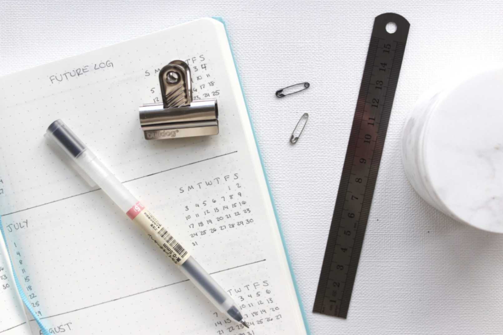 A top-down view of an agenda with a pen, ruler, and paper clips