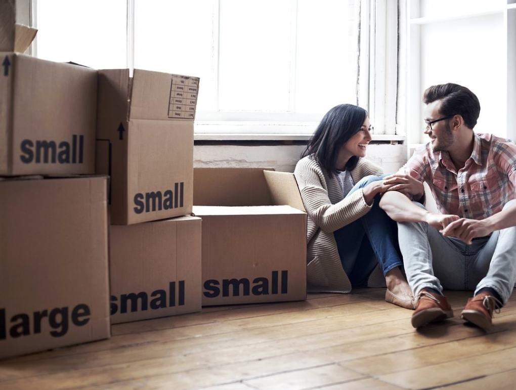 A couple sits on the floor next to several stacks of moving boxes